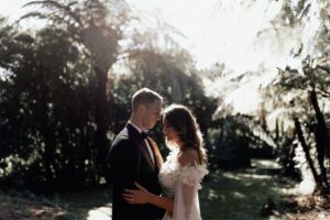 Testimonials | Vinka Design | Real Bridal Reviews from Our Clients | Candice and Michael face to face in dramatic outdoors forest area, the bride's bespoke dress with drop shoulder featuring in the light