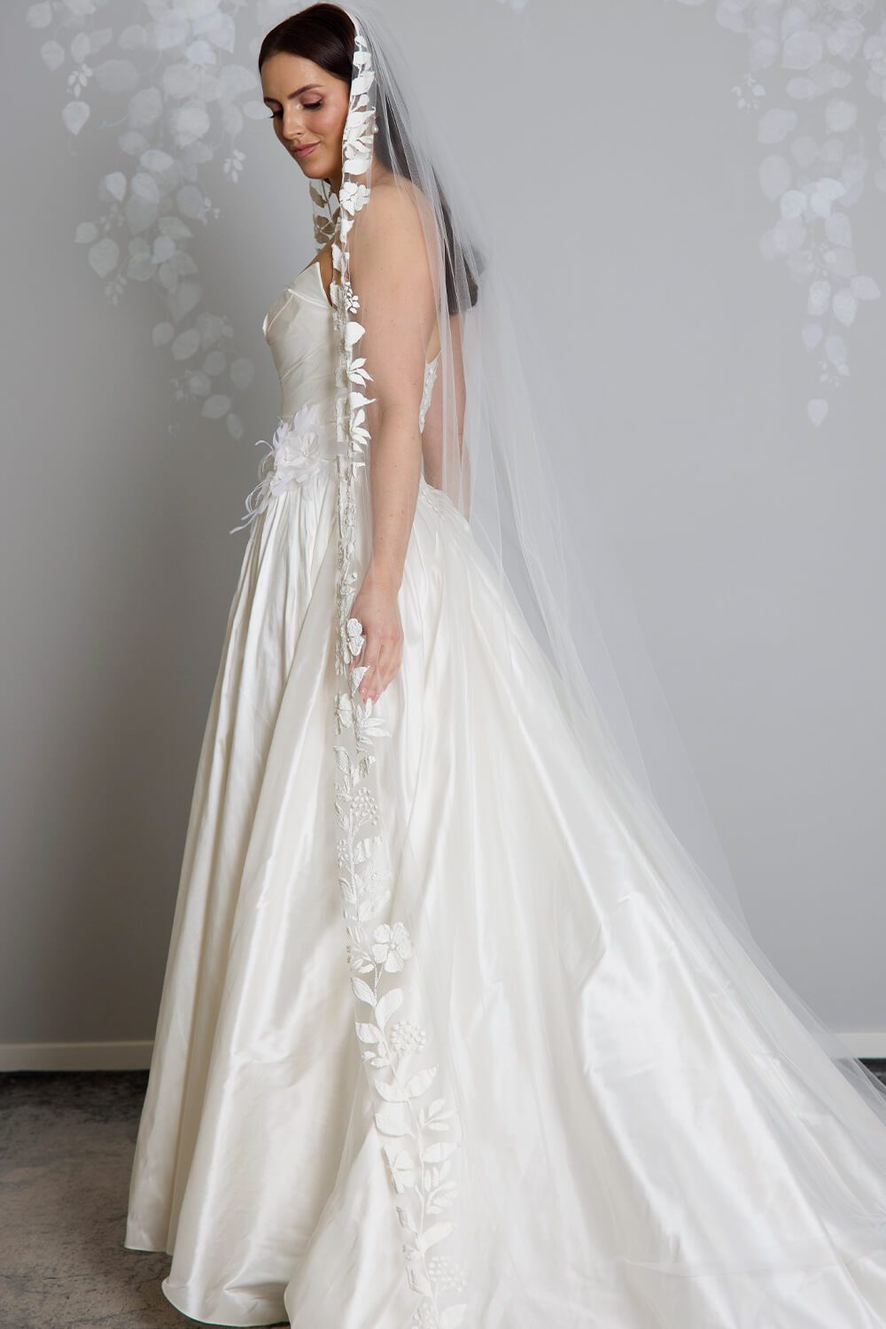 Fleur hand-painted bridal veil by Vinka Design, featuring delicate white floral motifs along the edge of a sheer tulle veil, styled with an ivory wedding gown.