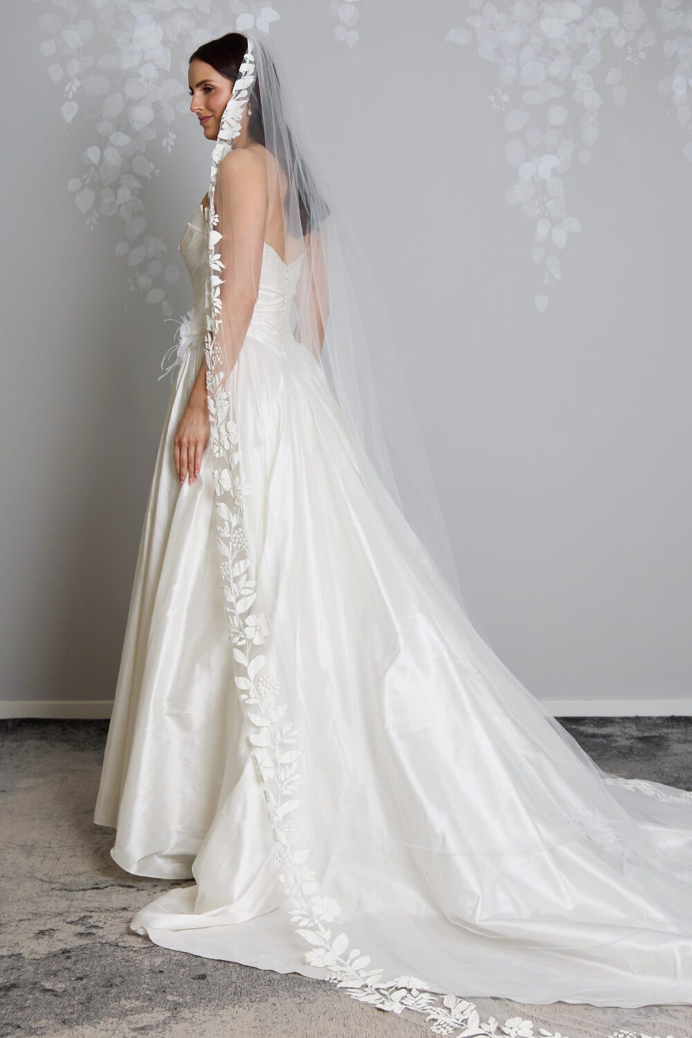 Fleur hand-painted bridal veil by Vinka Design, featuring delicate white floral motifs along the edge of a sheer tulle veil, styled with an ivory wedding gown.