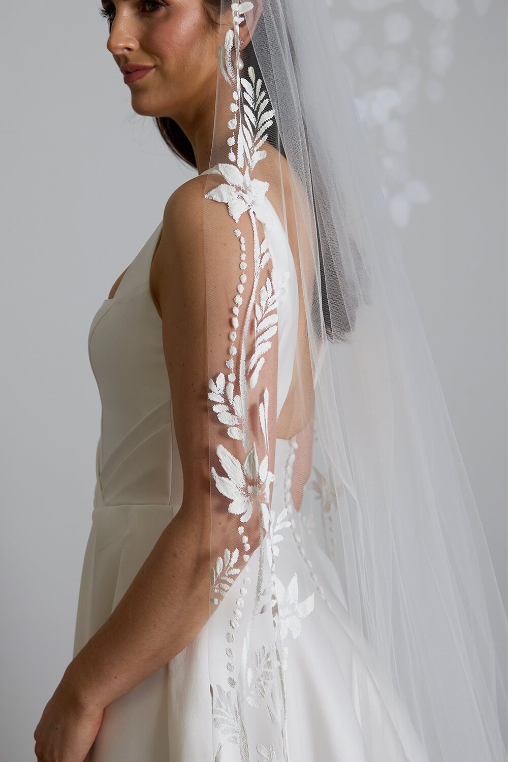 Flora hand-painted bridal veil by Vinka Design, featuring intricate white floral and botanical detailing along the edges of a sheer tulle veil, styled with an ivory wedding gown.