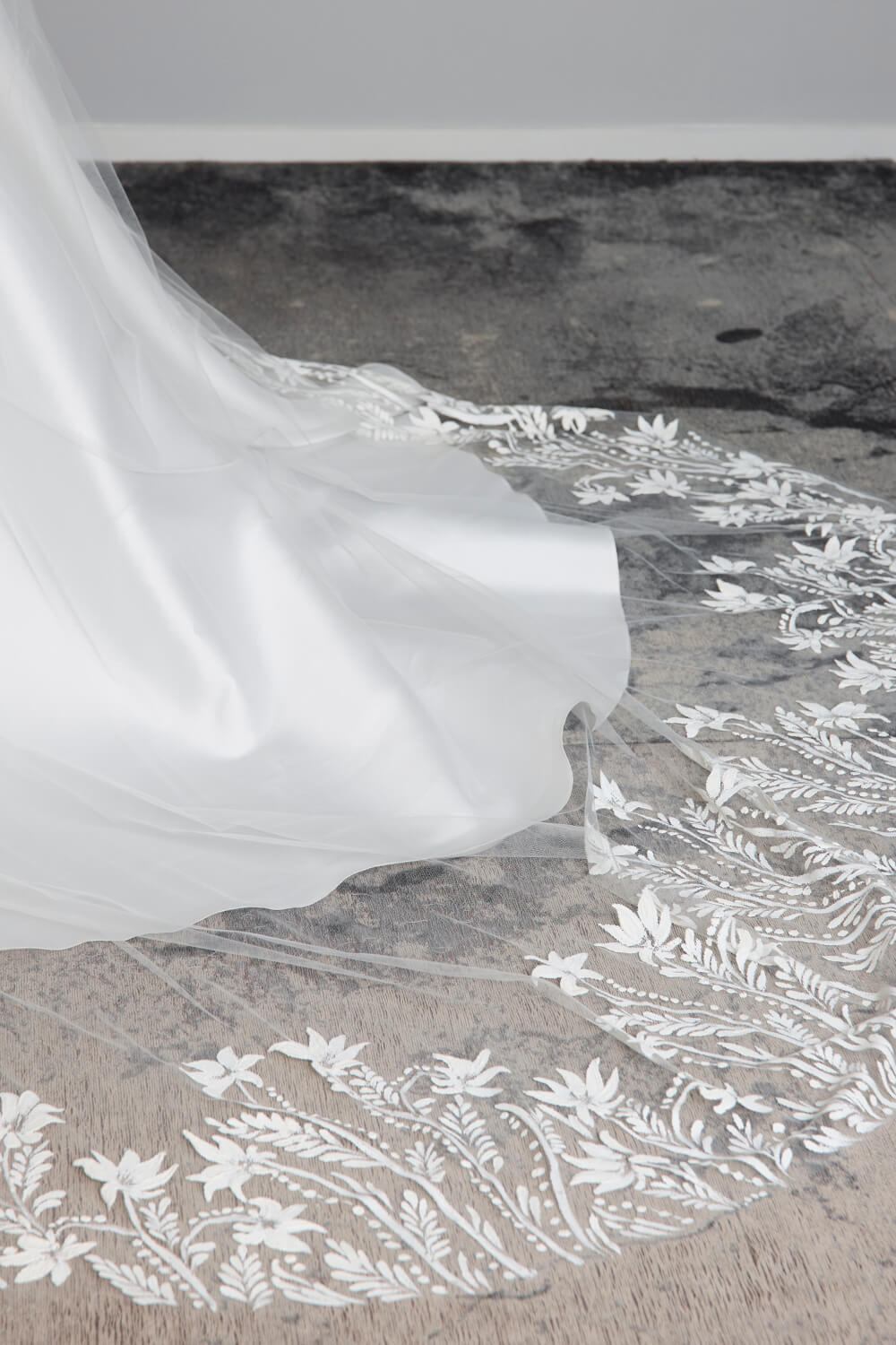 Flora hand-painted bridal veil by Vinka Design, featuring intricate white floral and botanical detailing along the edges of a sheer tulle veil, styled with an ivory wedding gown.