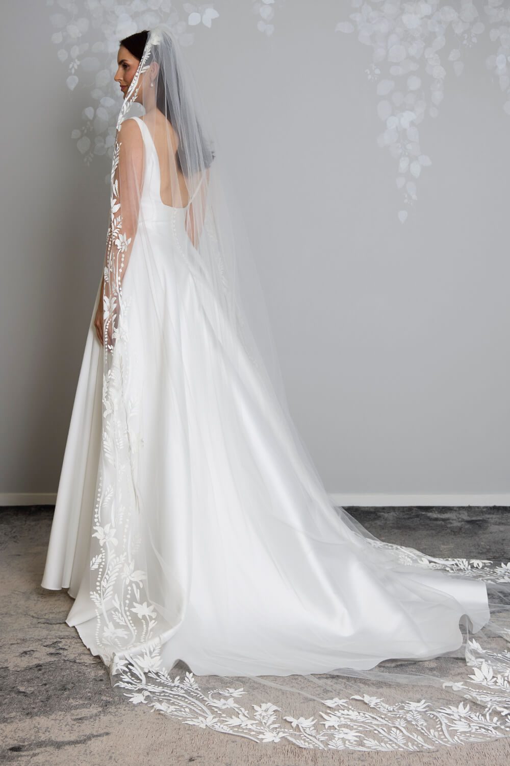 Flora hand-painted bridal veil by Vinka Design, featuring intricate white floral and botanical detailing along the edges of a sheer tulle veil, styled with an ivory wedding gown.