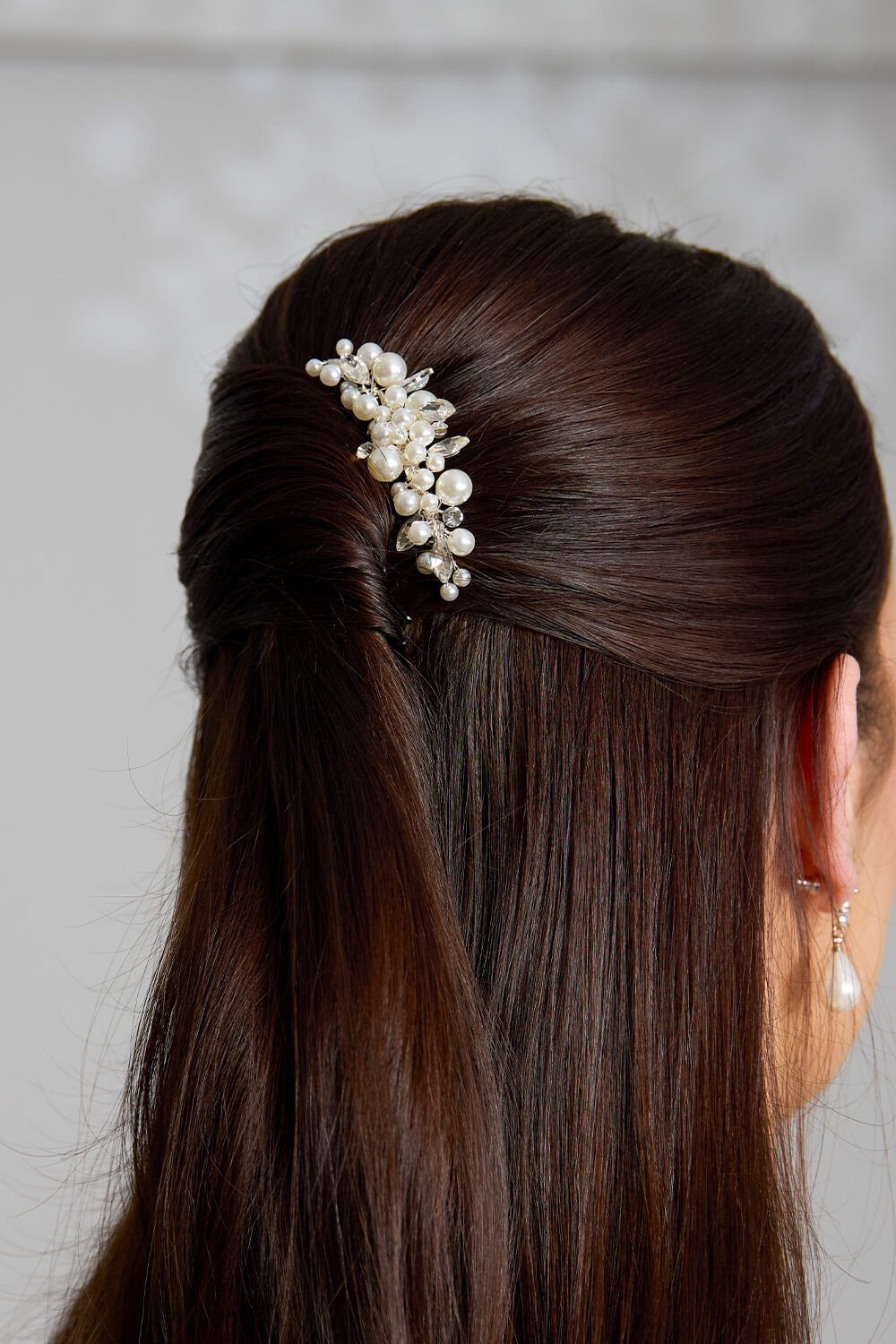 Close-up of the Liv bridal hair comb featuring mixed-size ivory pearls and marquise crystal leaves on a silver-finish setting, styled in a brunette model’s half-up hairstyle.