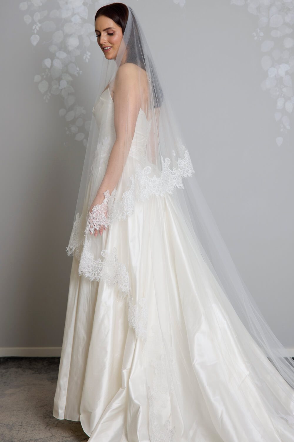Bride wearing the Marina two-tier ivory tulle veil, featuring intricate corded Chantilly lace edging, styled with a satin wedding gown.