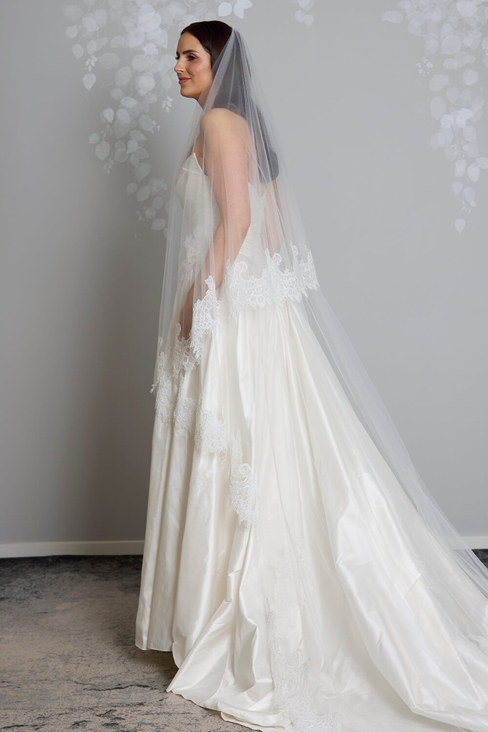 Bride wearing the Marina two-tier ivory tulle veil, featuring intricate corded Chantilly lace edging, styled with a satin wedding gown.