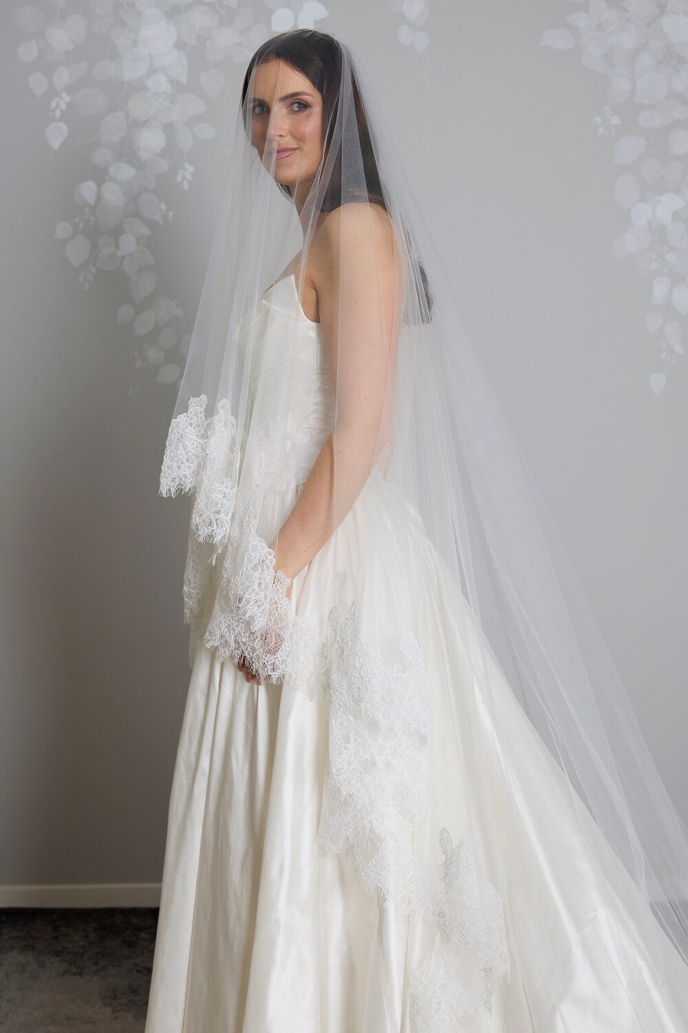 Bride wearing the Marina two-tier ivory tulle veil, featuring intricate corded Chantilly lace edging, styled with a satin wedding gown.