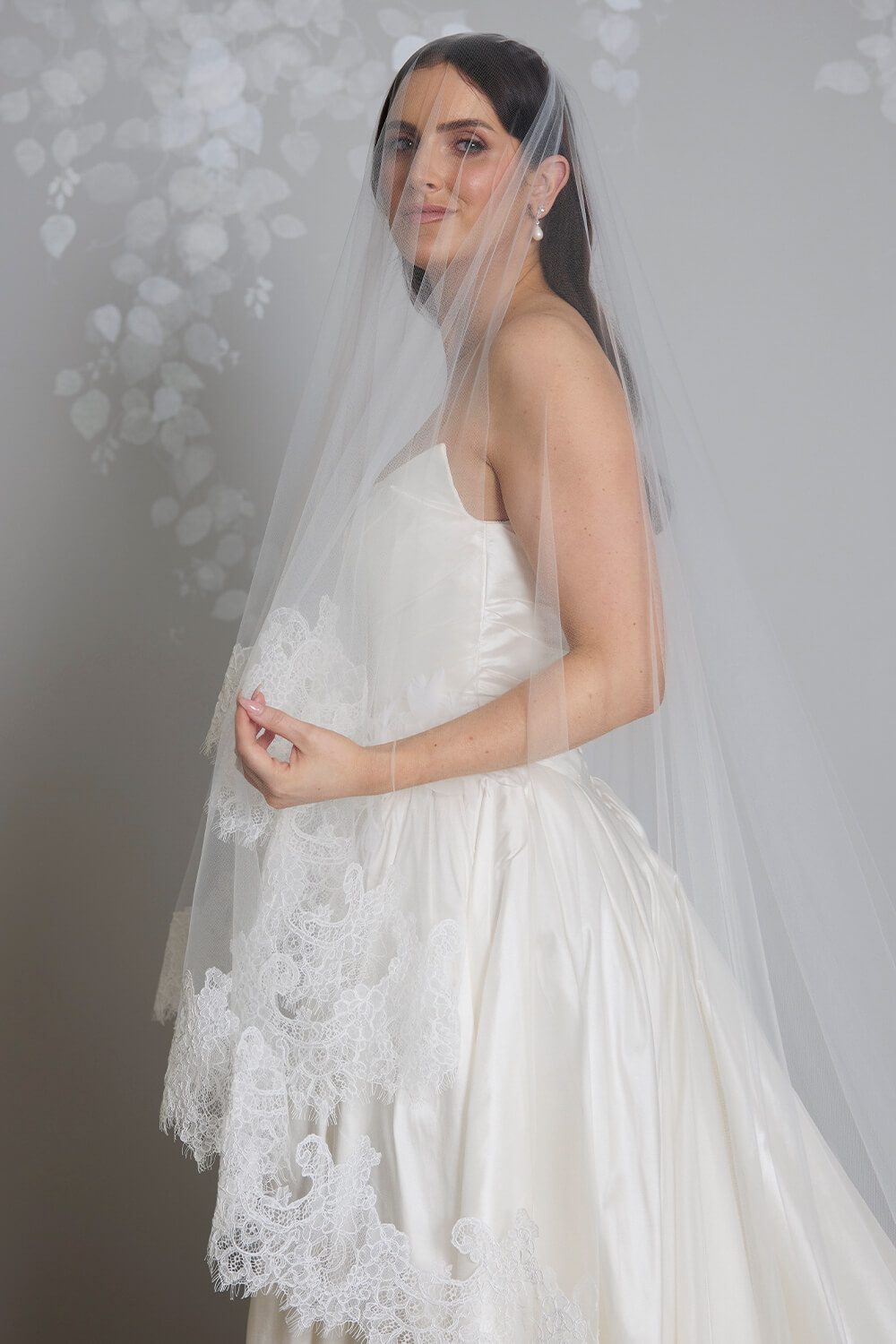 Bride wearing the Marina two-tier ivory tulle veil, featuring intricate corded Chantilly lace edging, styled with a satin wedding gown.