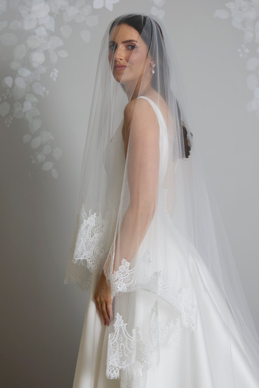 Bride wearing the Quinn two-tier ivory tulle wedding veil, featuring an intricate Chantilly lace edge and an 80cm blusher, styled with a satin wedding gown.