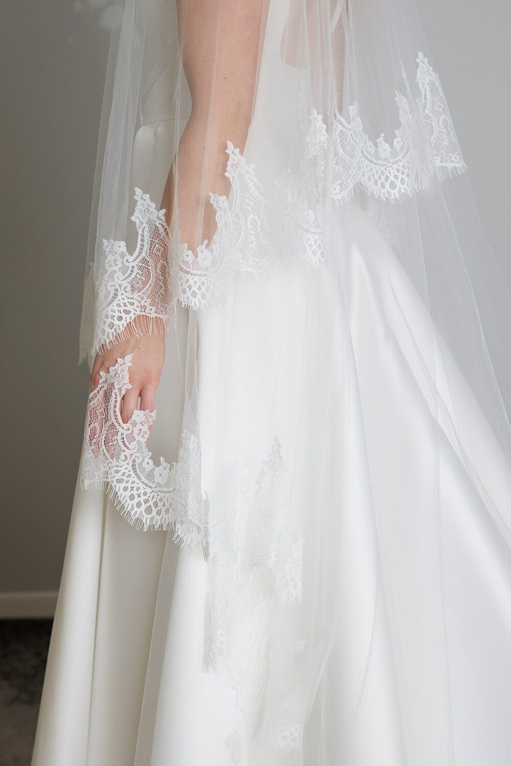 Bride wearing the Quinn two-tier ivory tulle wedding veil, featuring an intricate Chantilly lace edge and an 80cm blusher, styled with a satin wedding gown.