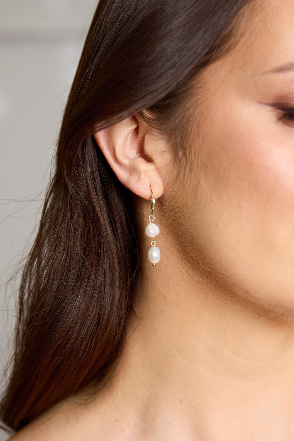 Gold-plated Rome freshwater pearl drop earrings featuring two lustrous white pearls, photographed worn against the ear.