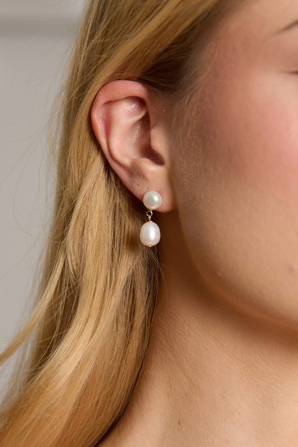 Close-up of the Sia gold freshwater pearl drop earrings, featuring a smaller round pearl above a larger teardrop-shaped pearl, worn by a blonde model.
